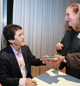 A seated man holding a pen hands a book to a broadly smiling woman